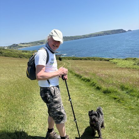 David, a white man and his dog on a sunny, grassy hilltop with the sea in the background