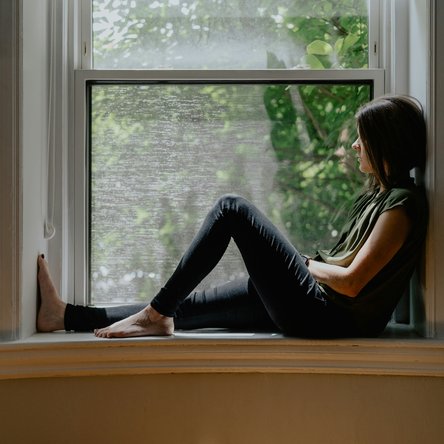 A woman sitting on a window ledge indoors, her hair is covering her face