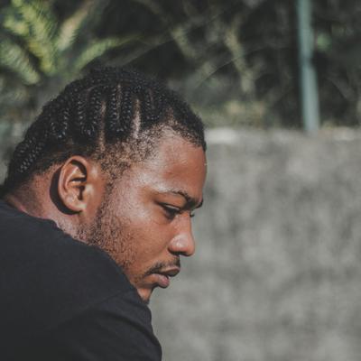A young man looks down at the ground with a serious expression on his face.