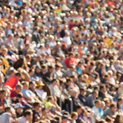 A blurred photo shows a crowd of men, possibly spectators sitting in the stands at a sporting event.