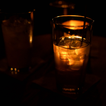 A group of three tall glasses filled with some kind of drink are pictured on a table in a dark bar.