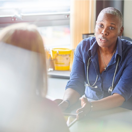 A female doctor with a stethoscope around her neck chats to a female patient.