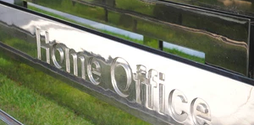 A long and large silver sign for the UK Home Office resting on top of some grass.