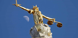 A gold statue of Lady Justice against a blue sky.
