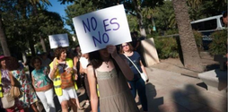 A group of women at a women's march. Some of the women are holding unreadable signs, the woman at the front of the group holds a sign that says 'no es no' in front of her face.