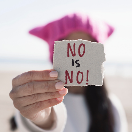 A woman holds up a piece of paper that says 'no is no!' in front of her face.