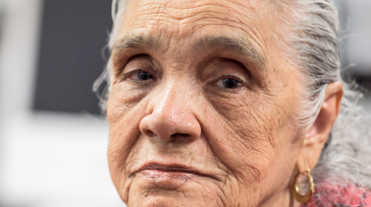 An older woman looks directly at the camera with a sad expression.