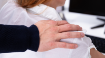 A man sexually harasses his female colleague by placing a hand on her shoulder.