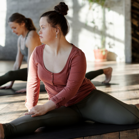 Two women do the splits on yoga mats in exercise clothes. They are looking forward.