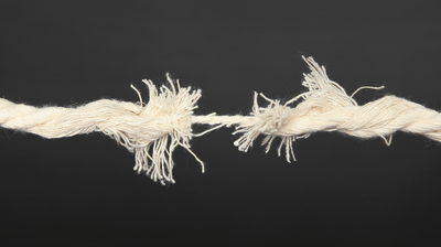 The image shows a photo of a piece of thick white string being pulled so taut that it is about to completely break. Just one strand is left, holding it together.