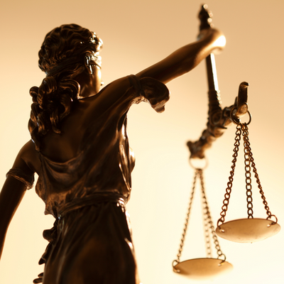 The image shows a photo of the back of a statue of Lady Justice, holding up scales in her right hand.