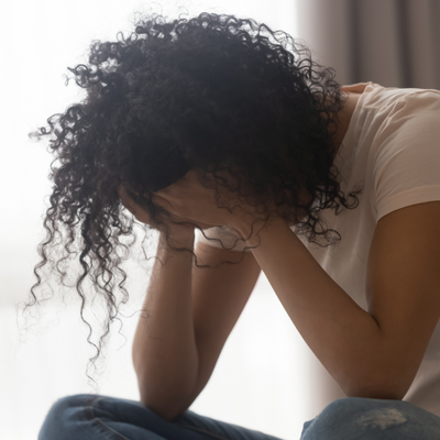A young woman bends over with her elbows on her knees and her face in her hands.