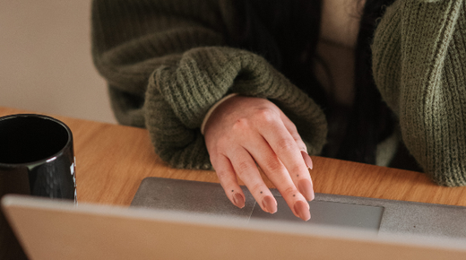 A shot of a laptop with a woman's hand scrolling on the touchpad.