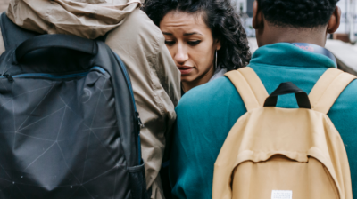 A young woman looks terrified as we see her confronted by two young men in the street. They have our backs to us so we can't see their faces.
