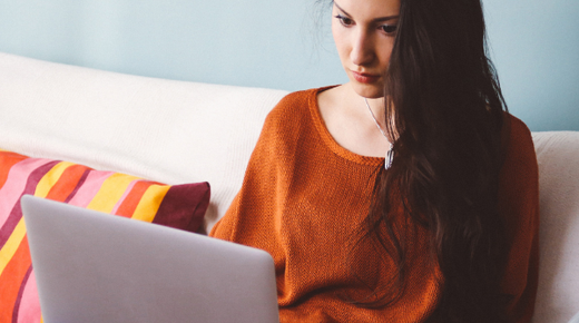 A young woman sits on a sofa and looks at a laptop.